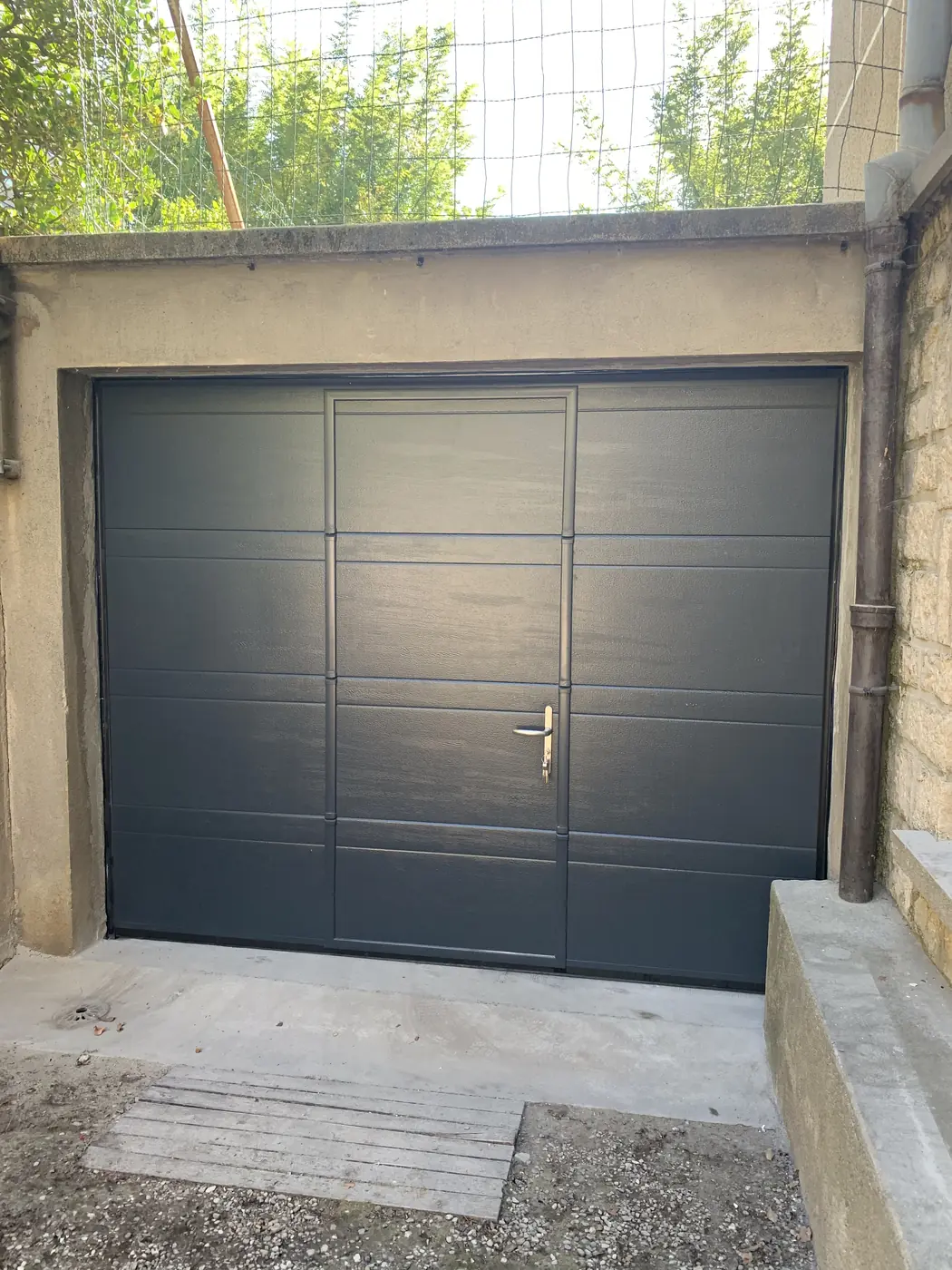 Porte de garage anthracite posée dans une façade en pierre