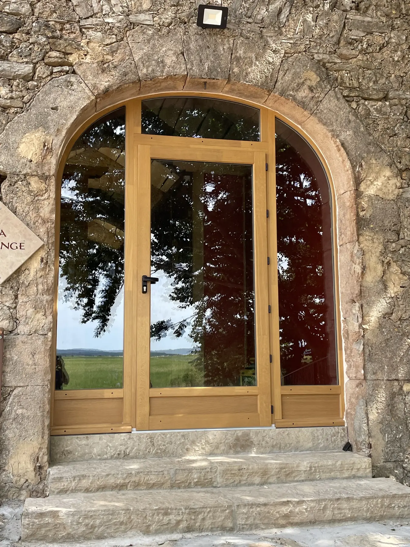 Porte-fenêtre en bois cintrée posée dans une façade en pierre